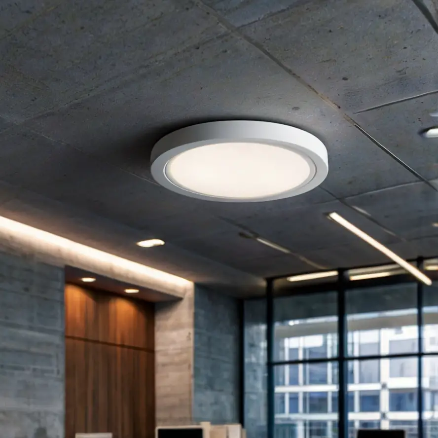 A white, circular passive infrared occupancy sensor installed on a ceiling in a modern office, blending seamlessly with the decor, indicating smart energy management.