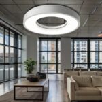 A white, circular passive infrared occupancy sensor installed on a ceiling in a modern office, blending seamlessly with the decor, indicating smart energy management.